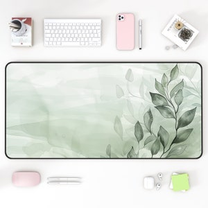May include: A green and white desk mat with a watercolor design of leaves. The mat has a black border.