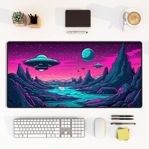 May include: A purple and pink galaxy themed mousepad with a blue planet, stars, and a flying saucer. The mousepad is on a white desk with a keyboard, mouse, and other office supplies.