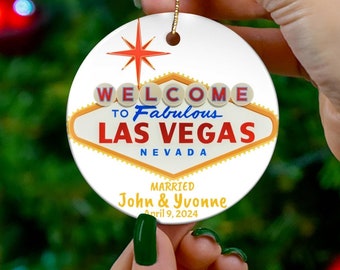 May include: White round Christmas ornament with a red, yellow, and blue graphic of the "Welcome to Fabulous Las Vegas" sign. The ornament also includes the text "Married John & Yvonne July 9, 2024".