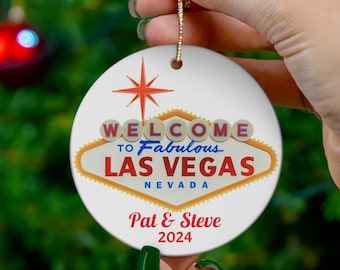 May include: A white ceramic Christmas ornament with a red, yellow, and blue design that says "Welcome to Fabulous Las Vegas, Nevada". The ornament also has the names "Pat & Steve" and the year "2024" printed on it.
