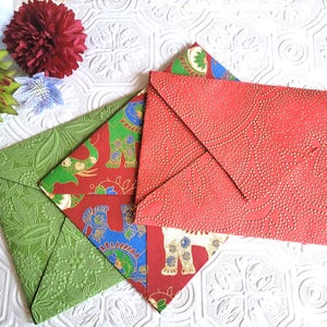 May include: Three decorative envelopes with different patterns. One envelope is green with a floral design, one is red with a gold elephant design, and one is red with a gold dot pattern.