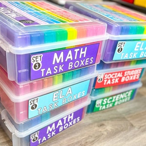 May include: Stack of clear plastic storage boxes with colorful labels. The labels read "Set 3 Math Task Boxes", "Set 3 ELA Task Boxes", "Set 2 Social Studies Task Boxes", "Set 2 Science Task Boxes", "Set 4 ELA Task Boxes", and "Set 4 Math Task Boxes".