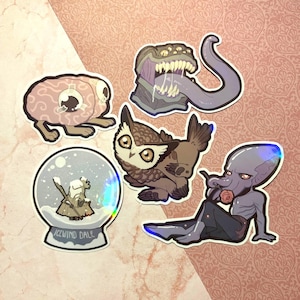 Puede incluir: Conjunto de cinco pegatinas de vinilo iridiscente con varias criaturas de fantasía. Las pegatinas incluyen una criatura parecida a un cerebro, un búho, una bola de nieve con una figura dentro, una criatura con tentáculos y una criatura de múltiples ojos con una lengua larga.