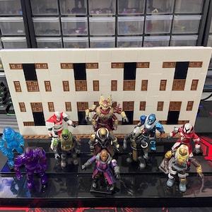 May include: A collection of 10 miniature action figures, including a red and black figure with a crown, a blue figure with a helmet, and a purple figure with a helmet. The figures are arranged on a black and white tiled surface.