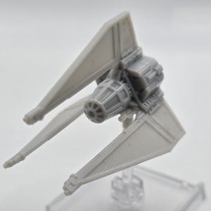 May include: A gray model of a TIE fighter spacecraft, featuring a central cockpit and two angled solar panels. The spacecraft is a miniature replica, showcasing detailed design elements and a textured surface. The model is set against a plain background.