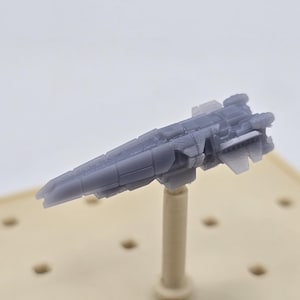 May include: A gray, futuristic spaceship model, mounted on a beige stand. The model has detailed features, including wings and multiple sections. The spaceship is a light gray color and appears to be made of plastic.