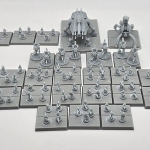 May include: A collection of gray miniature figurines and vehicles, likely for tabletop gaming. The set includes various small figures on square bases, along with larger, detailed vehicle models. The pieces are arranged on a white surface.