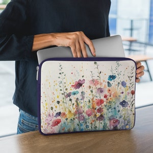 May include: A laptop sleeve with a watercolor design of colorful flowers on a white background. The sleeve has a purple zipper and is made of a durable material.