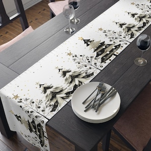 May include: A white table runner with a black and gray Christmas tree design, gold stars, and berries. The runner is placed on a dark wood table set for a meal, with plates, silverware, and wine glasses.