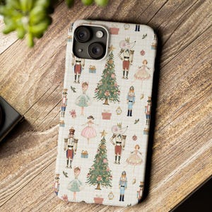 May include: A phone case with a festive Christmas-themed pattern. The design features illustrations of nutcrackers, ballerinas, Christmas trees, and mice. The case has a light background with a grid pattern.