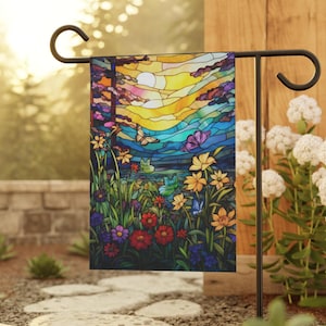 May include: A colourful stained glass garden flag featuring a sunset scene and flowers. The flag is attached to a black metal garden flag stand.