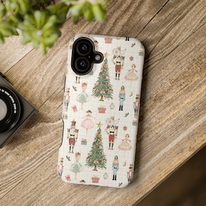 May include: A white smartphone case featuring a repeating pattern of Christmas trees, nutcrackers, ballerinas, and mouse characters in uniform. The design includes small gift boxes and ornaments on a subtle grid background with a black camera cutout.