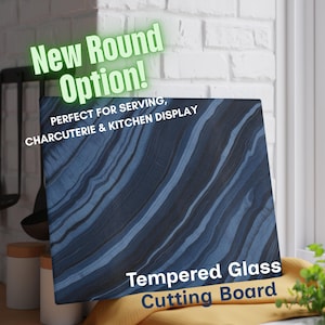 May include: A square tempered glass cutting board featuring a dark blue and black diagonal marble-like pattern. The text on the board reads New Round Option! PERFECT FOR SERVING, CHARCUTERIE & KITCHEN DISPLAY and Tempered Glass Cutting Board.