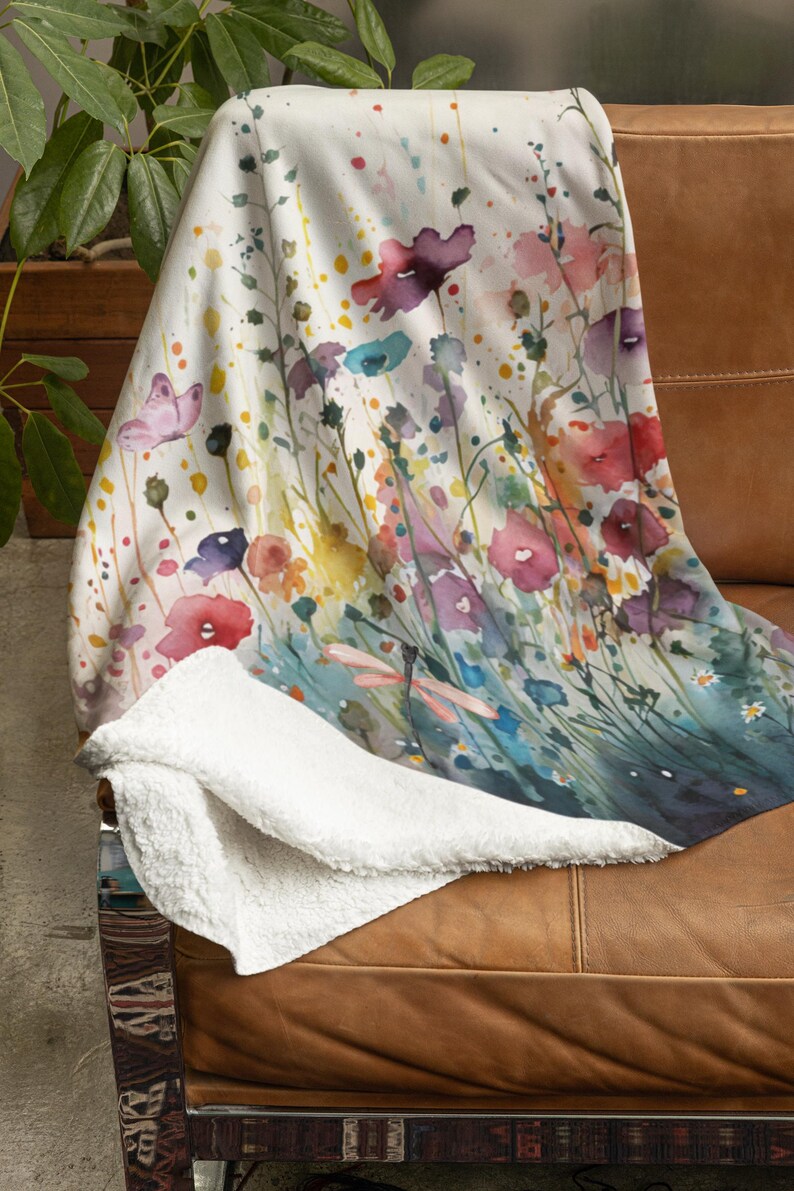 May include: A white throw blanket with a watercolor design of colorful flowers and a dragonfly. The blanket has a soft, fuzzy texture.