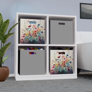 May include: A white four-cube storage unit featuring two solid gray fabric storage bins and two fabric storage bins decorated with a colorful watercolor-style floral print featuring red, blue, and yellow flowers and a dragonfly.