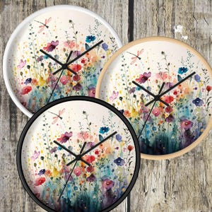 May include: Three round wall clocks with a watercolor design of colorful flowers and a dragonfly. The clocks have black hands and a white background.