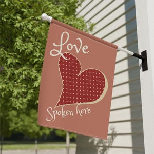 May include: A pink garden flag with a red heart with white polka dots and the text "Love Spoken Here" in a cream colour.
