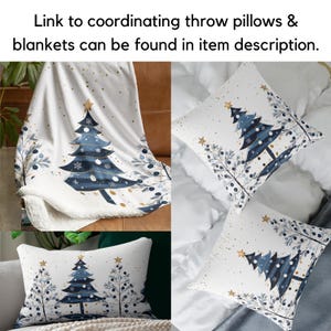May include: A white throw blanket with a blue and gold Christmas tree design. The blanket is folded and displayed on a couch. Two throw pillows with the same design are also shown.