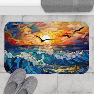 May include: A colorful stained glass style bath mat with a sunset over the ocean and three birds flying in the sky. The mat is blue, yellow, orange, and red.