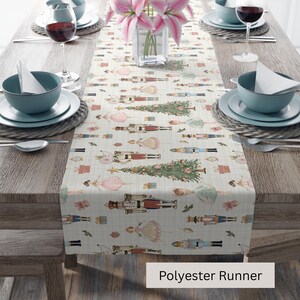 May include: A cream-colored polyester table runner with a repeating pattern of Christmas trees, nutcrackers, and ballerinas. The runner is set on a wooden table with place settings and a vase of pink flowers. The text "Polyester Runner" is visible.