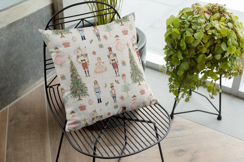 May include: A decorative square pillow with a festive Nutcracker theme. The pillow features a repeating pattern of Nutcracker soldiers, ballerinas, Christmas trees, and gift boxes in soft pastel colors on a cream background. The pillow is placed on a black metal chair.