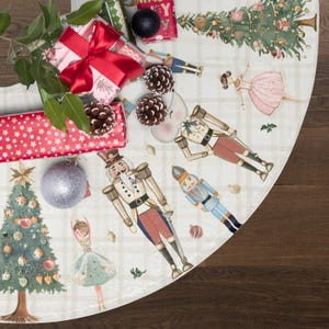 May include: A circular Christmas tree skirt featuring a white and beige plaid pattern with watercolor illustrations of nutcrackers, ballerinas, and decorated pine trees. The fabric is adorned with pinecones, gift boxes, and ornaments.