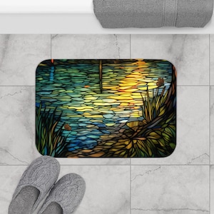 Puede incluir: Una alfombra de ba&ntilde;o estilo vitral con un dise&ntilde;o colorido de un lago con un reflejo de puesta de sol. La alfombra presenta tonos de azul, verde, amarillo y marr&oacute;n.