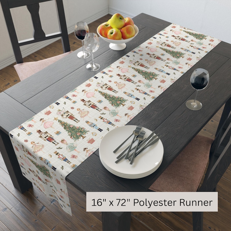 May include: A cream-colored polyester table runner, 16 inches wide and 72 inches long, featuring a repeating pattern of nutcrackers, Christmas trees, and ballerinas. The runner is displayed on a dark wooden table, set with plates, silverware, and wine glasses.