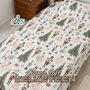 May include: A cream-colored bedspread with a repeating pattern of Christmas trees, nutcrackers, and ballerinas. The text "3 SIZES" is in the upper left corner. The words "Super Soft VELVETEEN" are printed across the bottom.
