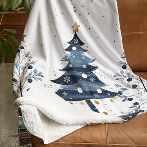 May include: A white fleece throw blanket with a blue and gold Christmas tree design. The blanket has a white sherpa lining.