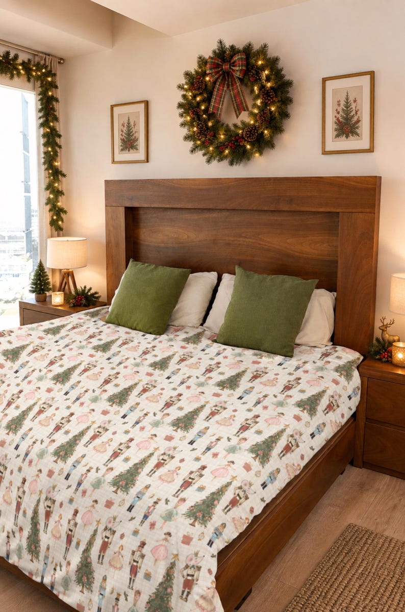 May include: A white bedspread featuring a repeating pattern of nutcracker figures, Christmas trees, and small gift boxes. The bedding is placed on a wooden bed frame with two olive green square pillows and two white rectangular pillows.