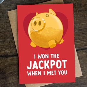 Könnte beinhalten: Rote Karte mit einem goldenen Sparschwein, das mit Geld gefüllt ist, in einem roten Herzen. Der Text lautet "Ich habe den JACKPOT gewonnen, als ich dich getroffen habe".