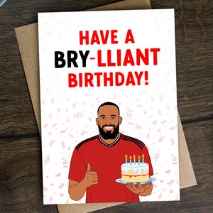 May include: A birthday card with the text "HAVE A BRY-LLIANT BIRTHDAY!". The card features an illustration of a person holding a cake with lit candles. The person is wearing a red shirt and giving a thumbs up.