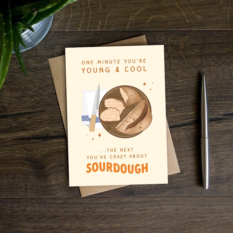 Pode incluir: Um cart&atilde;o de felicita&ccedil;&otilde;es com um fundo amarelo claro apresenta uma ilustra&ccedil;&atilde;o de desenho animado de uma t&aacute;bua de cortar de madeira com quatro fatias de p&atilde;o de fermenta&ccedil;&atilde;o natural e uma faca de manteiga. O texto no cart&atilde;o diz "One minute you're young & cool... the next you're crazy about sourdough."