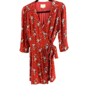 May include: A red wrap dress with a white floral print. The dress has a V-neckline and 3/4 sleeves. The dress is tied at the waist with a sash.