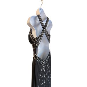 Puede incluir: Un vestido de noche negro con lentejuelas y un dise&ntilde;o de espalda cruzada. El vestido tiene un corpi&ntilde;o ajustado y una falda fluida.