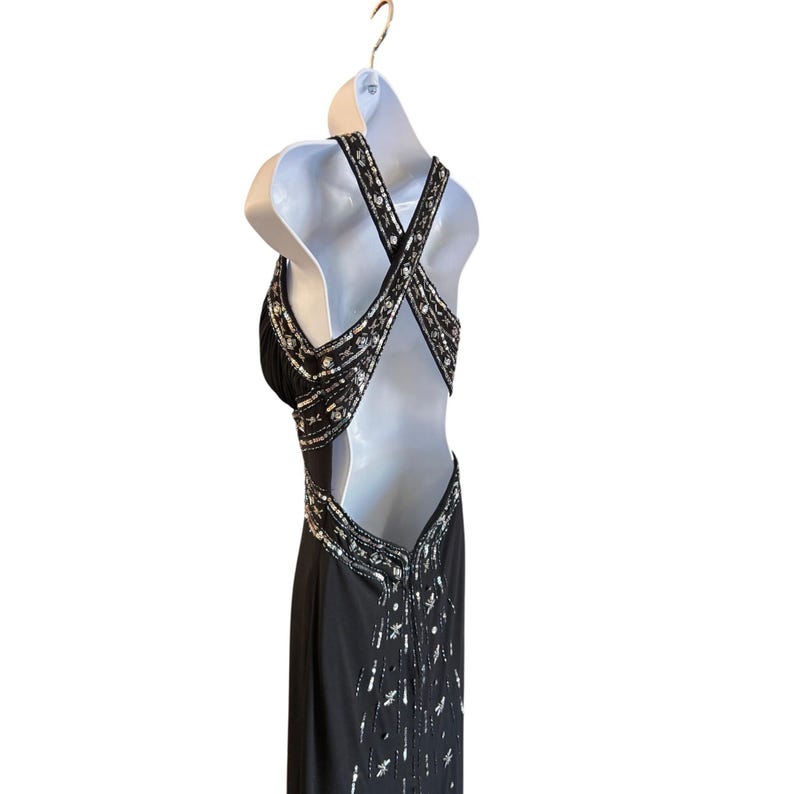 Puede incluir: Un vestido de noche negro con lentejuelas y un dise&ntilde;o de espalda cruzada. El vestido tiene un corpi&ntilde;o ajustado y una falda fluida.