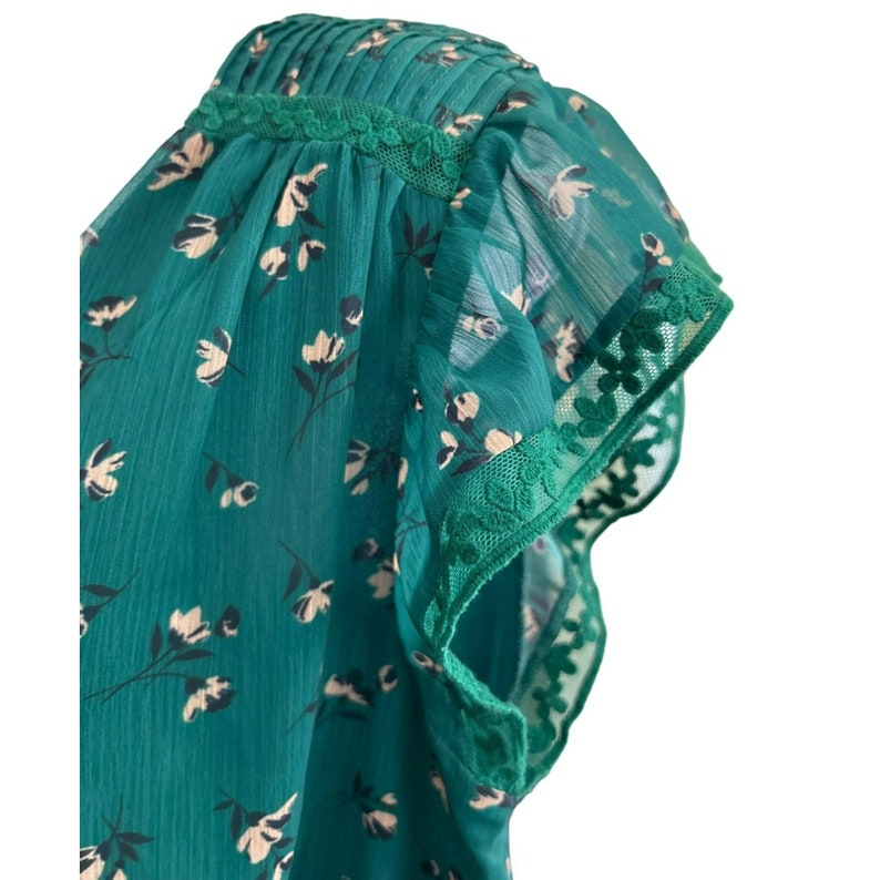 May include: A green floral print blouse with a ruffled, sheer sleeve trimmed with white lace.
