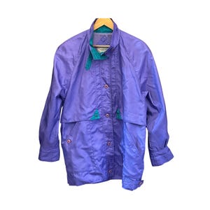 May include: A vintage purple jacket with a teal collar and accents. The jacket has a button-up front, two pockets, and a collared neckline. The jacket is hanging on a wooden hanger.