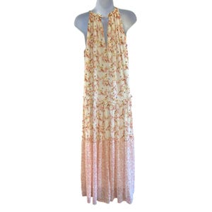 Pode incluir: Um vestido maxi branco com estampa floral em tons de rosa e laranja. O vestido tem um decote halter e uma saia em camadas.