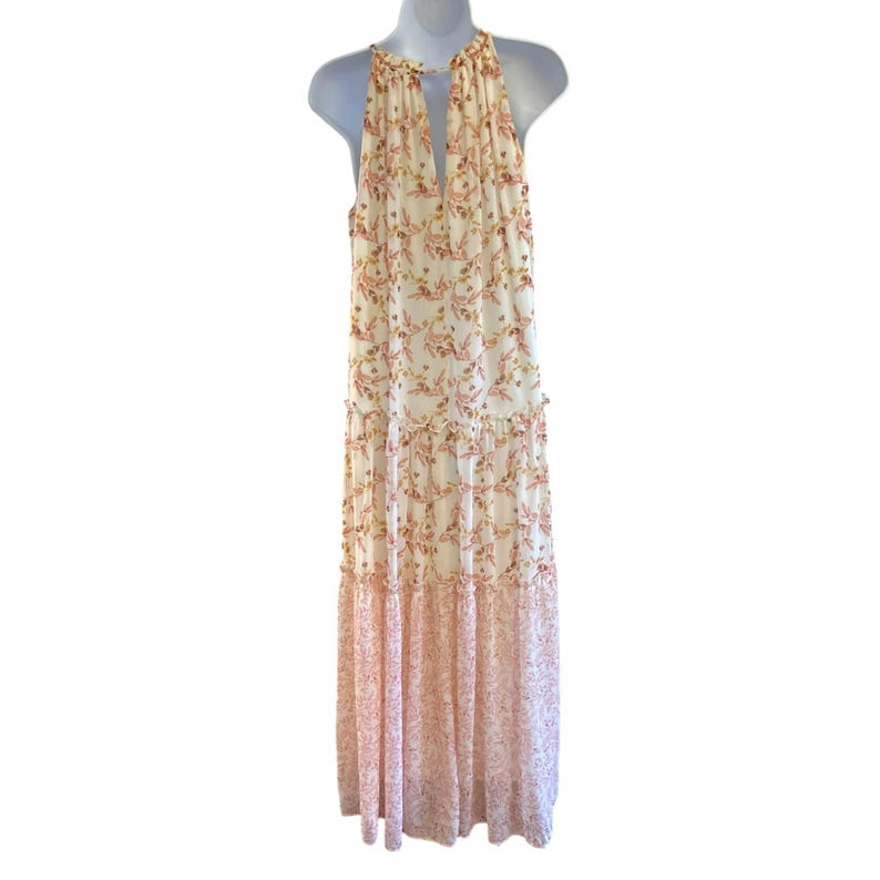 Pode incluir: Um vestido maxi branco com estampa floral em tons de rosa e laranja. O vestido tem um decote halter e uma saia em camadas.