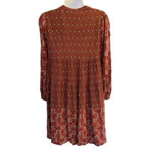 Puede incluir: Un vestido largo de manga larga y de varios niveles con un patr&oacute;n geom&eacute;trico en tonos rojos, marrones y blancos. El vestido tiene un escote en V y una cintura fruncida.