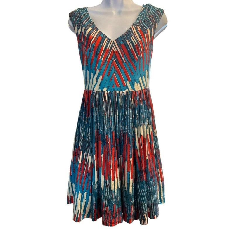 Op de afbeelding: Een mouwloze jurk met een V-hals en een kleurrijke abstracte print in tinten blauw, rood en wit. De jurk heeft een aansluitend bovenlijf en een zwierige rok.