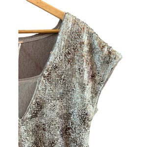 May include: A sleeveless top with a brown knit base and a silver sequined overlay. The sequins are in a snake skin pattern.