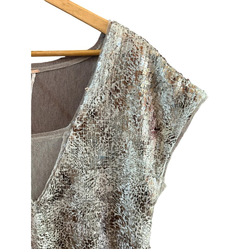 May include: A sleeveless top with a brown knit base and a silver sequined overlay. The sequins are in a snake skin pattern.