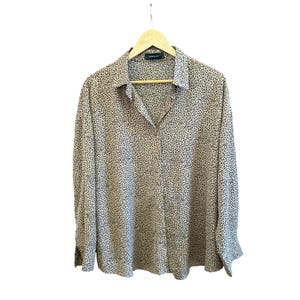 Puede incluir: Una camisa beige con botones y estampado de leopardo en blanco y negro. La camisa tiene mangas largas y cuello.