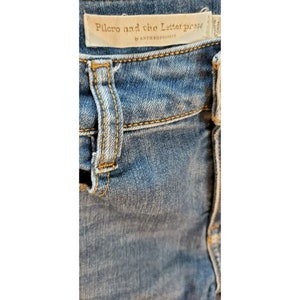 May include: Close-up of blue denim jeans with a brown leather patch that reads "Pilcro and the Letterpress by Anthropologie".