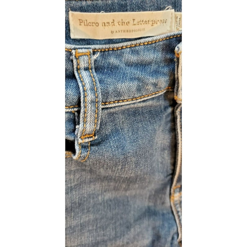 May include: Close-up of blue denim jeans with a brown leather patch that reads "Pilcro and the Letterpress by Anthropologie".
