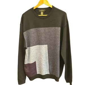 May include: A black, gray, and blue long-sleeved sweater with a geometric pattern. The sweater has a crew neck and is made of a soft, comfortable material.