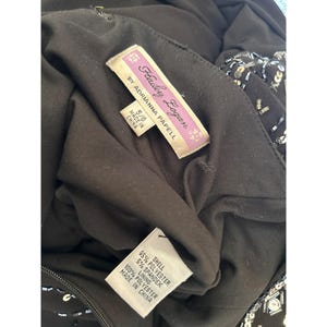 Puede incluir: Vestido negro sin mangas con lentejuelas y abalorios. El vestido tiene un escote redondo y una silueta ajustada. La etiqueta dice "Hailey Logan by Adrianna Papell" e indica que el vestido est&aacute; hecho en China.